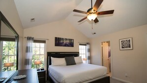 Quarto com cama, luminárias de cabeceira, ventoinha no teto e janela com cortinas.