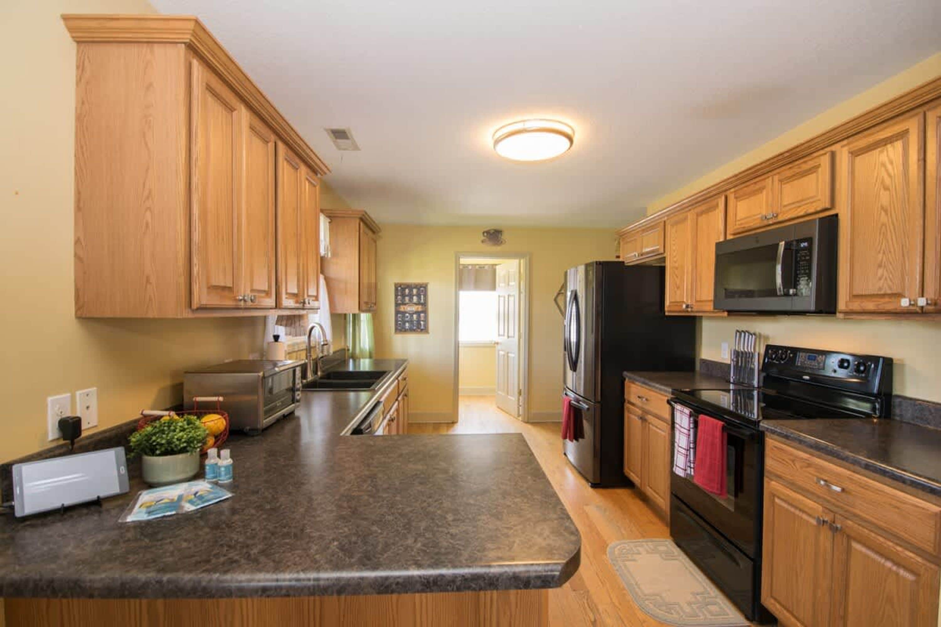 A kitchen with wooden cabinets, a granite countertop, a refrigerator, a microwave, and a stove.