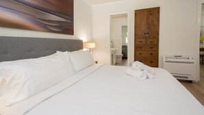 A hotel room with a large bed, a wooden wardrobe, a bedside table with a lamp, and an air conditioning unit. - Lakeview 1BR Condo w Deck Walk to Village (Flat Rock)