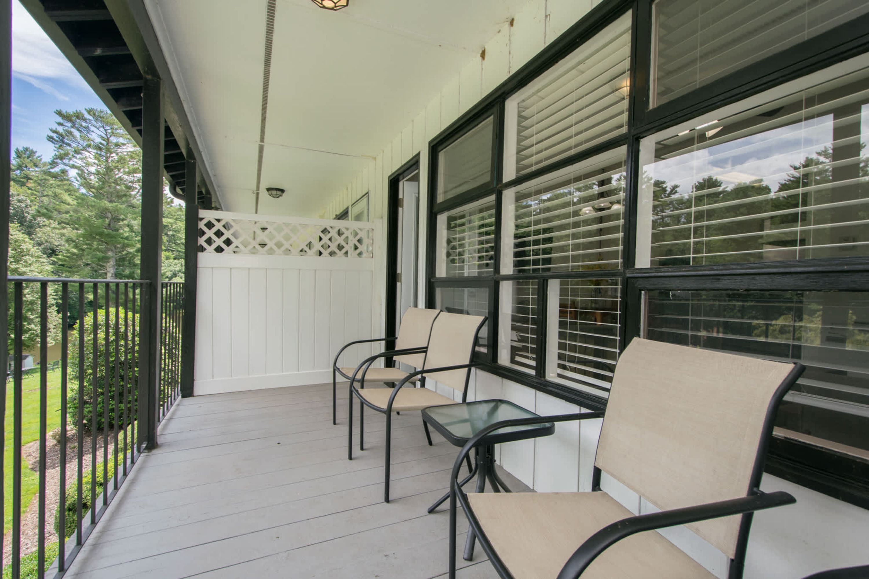 A covered porch with a white railing, two chairs, and a small table.