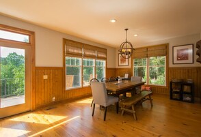 Un comedor amplio con mesa y sillas de madera, ventanas grandes con persianas y una araña.