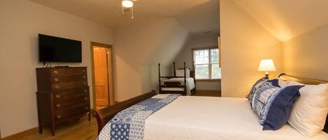 A bedroom with a bed, a dresser, a television, a ceiling fan, and a window.