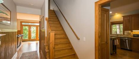 A wooden staircase leading to a second floor, a kitchen with wooden cabinets, and a large window.