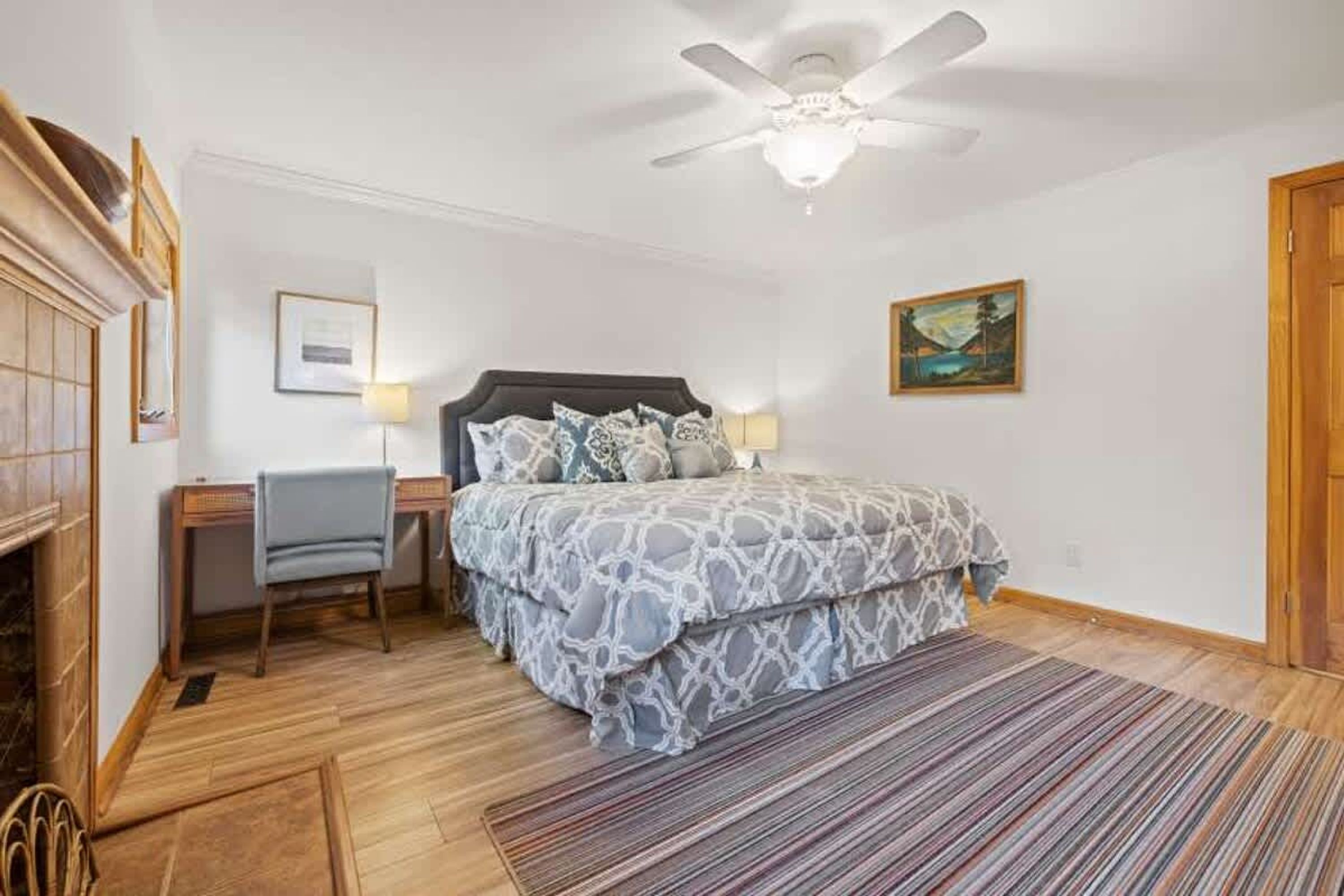 A bedroom with a bed, desk, chair, and a ceiling fan.