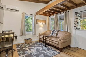 Una sala de estar acogedora con un sofá, una mesa de comedor con sillas, una lámpara y una ventana con cortinas.