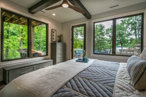 A bedroom with large windows, a bed, a dresser, and a view of the outdoors. - Epic 5BR w Double Living Areas On Lake Lure (Lake Lure)