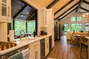 Una cocina moderna con un ventanal grande, vigas de madera en el techo y un comedor con mesa y sillas.
