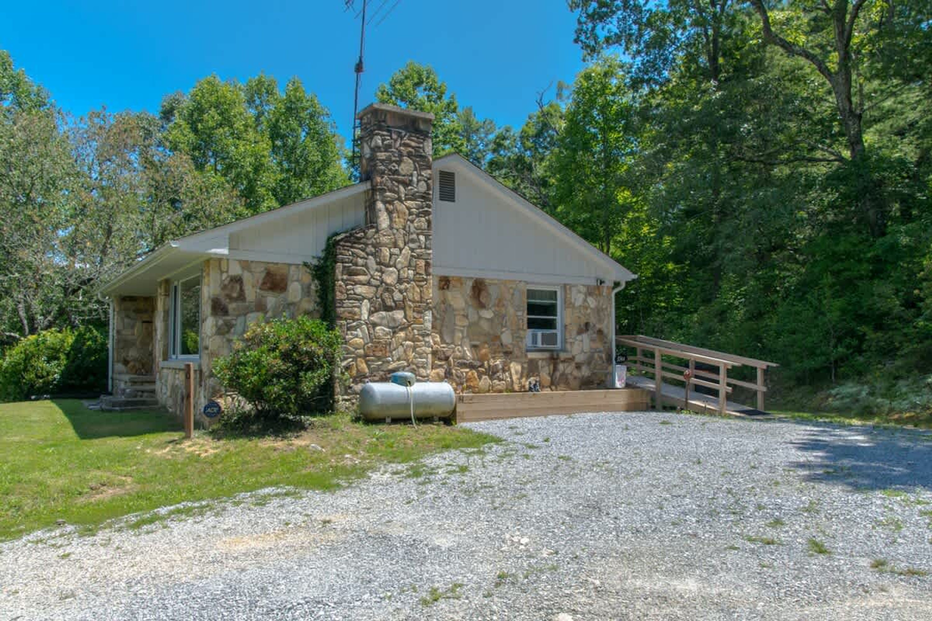 A stone building with a chimney, a covered porch, and a gravel driveway.