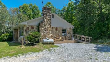 A stone building with a chimney, a covered porch, and a gravel driveway.