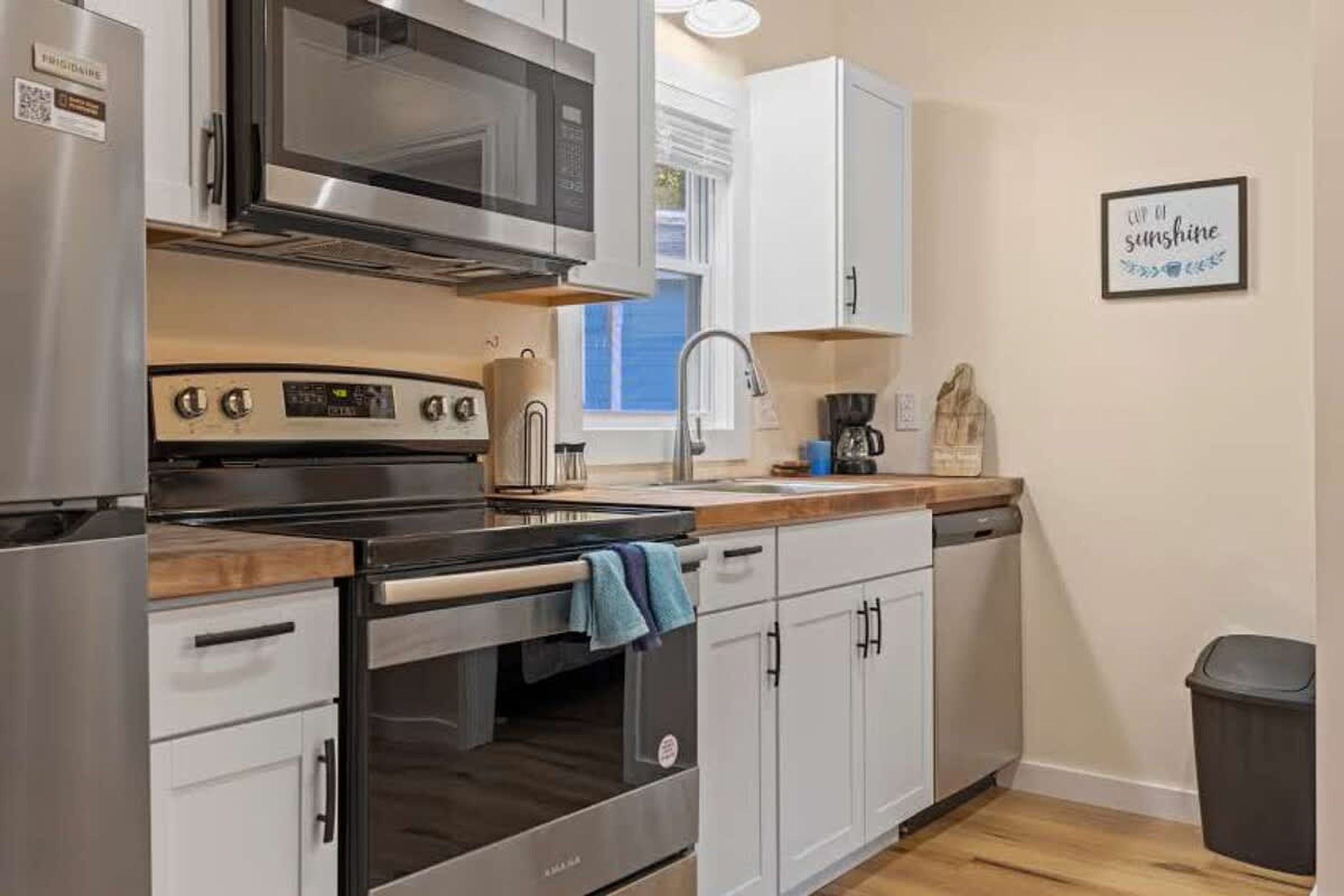 A modern kitchen with stainless steel appliances, white cabinetry, and a wooden countertop.
