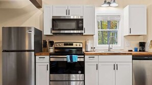 A modern kitchen with stainless steel appliances, white cabinets, and a window providing natural light. - Accessible 1BR Cottage w Firepit Near Trails (Hendersonville)