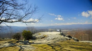 A rocky landscape with a metal fence and a viewing platform overlooking distant mountains. - Accessible 1BR Cottage w Firepit Near Trails (Hendersonville)