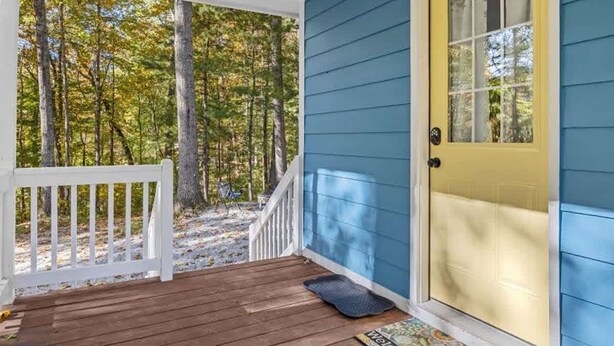 A porch with a wooden deck, a yellow door, and a view of a forest. - Cozy 1BR Cottage w Firepit Close to Downtown (Hendersonville)