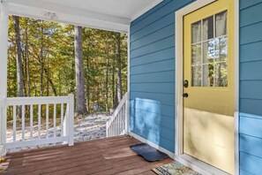 A porch with a wooden deck, a yellow door, and a view of a forest. - Cozy 1BR Cottage w Firepit Close to Downtown (Hendersonville)
