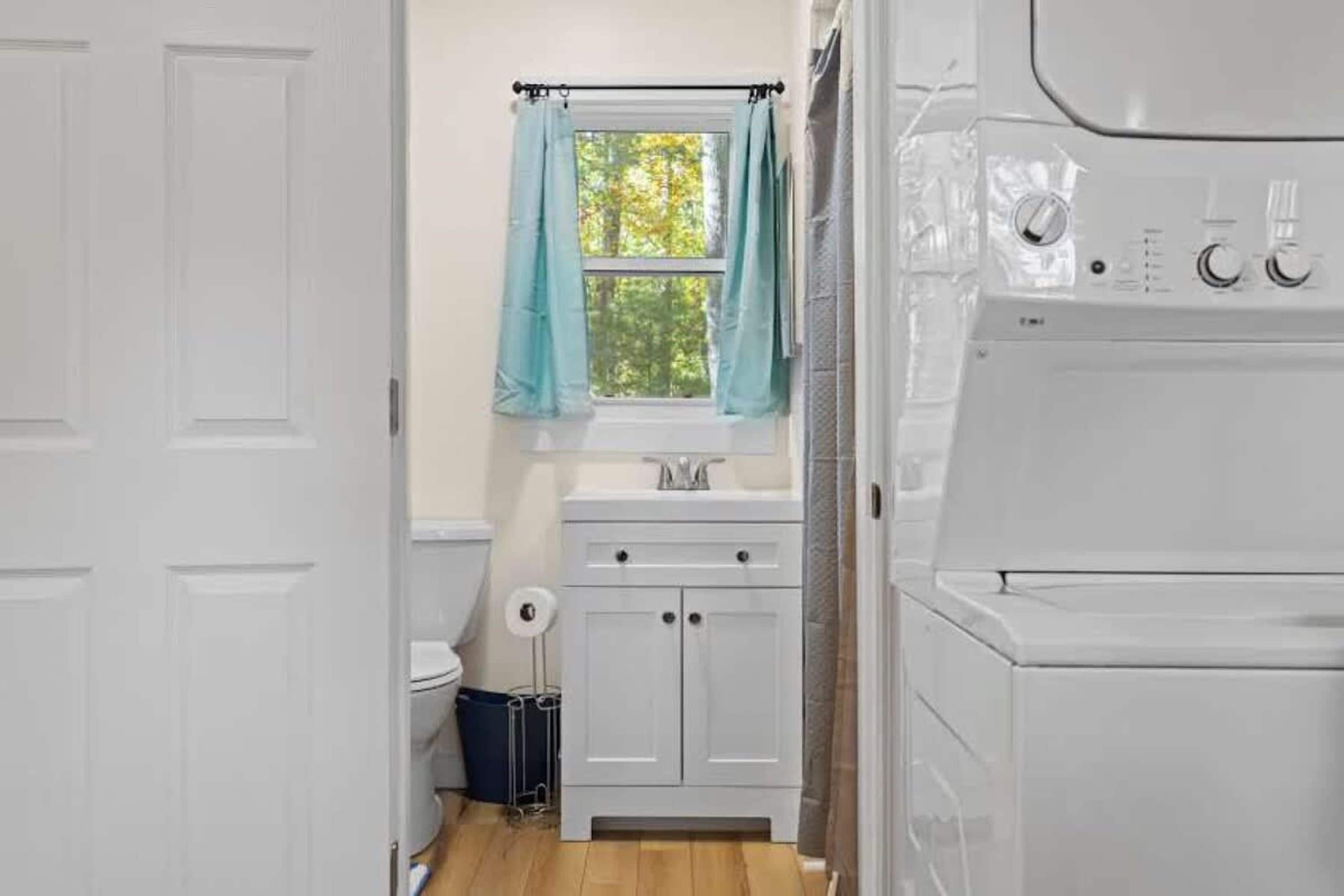A laundry room with a washing machine, a sink, and a window with curtains.