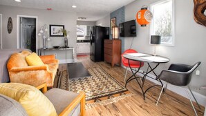 A modern living room with a sofa, chairs, a dining table, and a kitchen in the background. - Cheerful Studio w Patio Steps From Everything (Asheville)