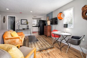 A modern living room with a sofa, chairs, a dining table, and a kitchen in the background. - Cheerful Studio w Patio Steps From Everything (Asheville)