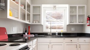A kitchen with white cabinets, a black countertop, a red appliance, and a window with a view of a wooden structure. - Cheerful Studio w Patio Steps From Everything (Asheville)