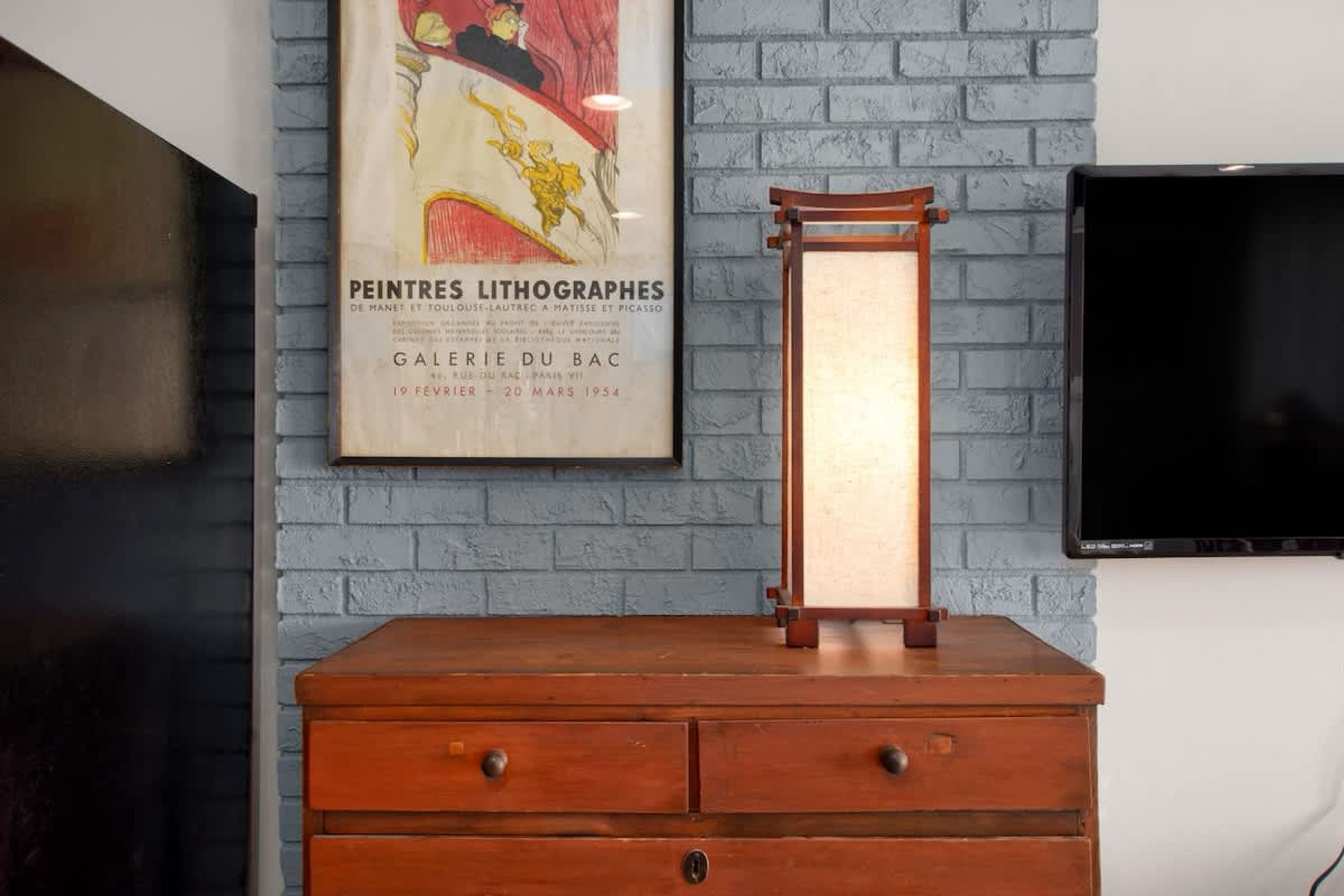 A vintage wooden dresser with drawers, a framed poster on the wall, and a television mounted on the wall.