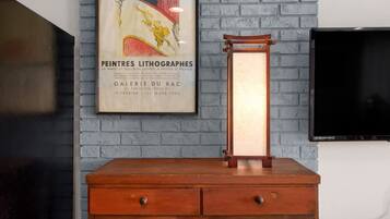 A vintage wooden dresser with drawers, a framed poster on the wall, and a television mounted on the wall.