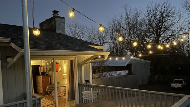 A wooden deck with a table and chairs, string lights, and a covered area with a chair and table. - Cheerful Studio w Patio Steps From Everything (Asheville)