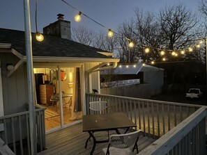A wooden deck with a table and chairs, string lights, and a covered area with a chair and table. - Cheerful Studio w Patio Steps From Everything (Asheville)