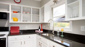 A modern kitchen with white cabinets, a black countertop, and a window providing natural light. - Cheerful Studio w Patio Steps From Everything (Asheville)