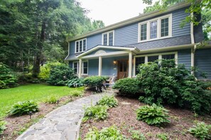 A two-story house with a stone pathway leading to the front door, surrounded by lush greenery and trees. - Historic 4BR Colonial w Pool Table Fire Pit (Hendersonville)