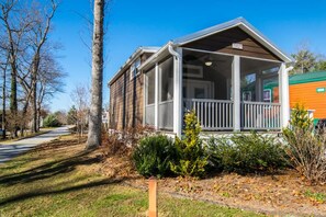 A single-story mobile home with a porch, surrounded by trees and a clear sky. - Cozy 1BR Tiny Home w Pool Access Free Tix (Flat Rock)