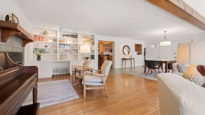 Un vaste salon doté d’un parquet, d’un piano, d’un canapé blanc et d’un coin repas avec une table et des chaises.
