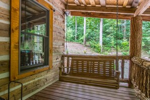 A wooden cabin with a porch, a swing, and a large window overlooking a forest. - Epic 1BR Cabin w Outdoor Fireplace 5 Min to Town (Saluda)