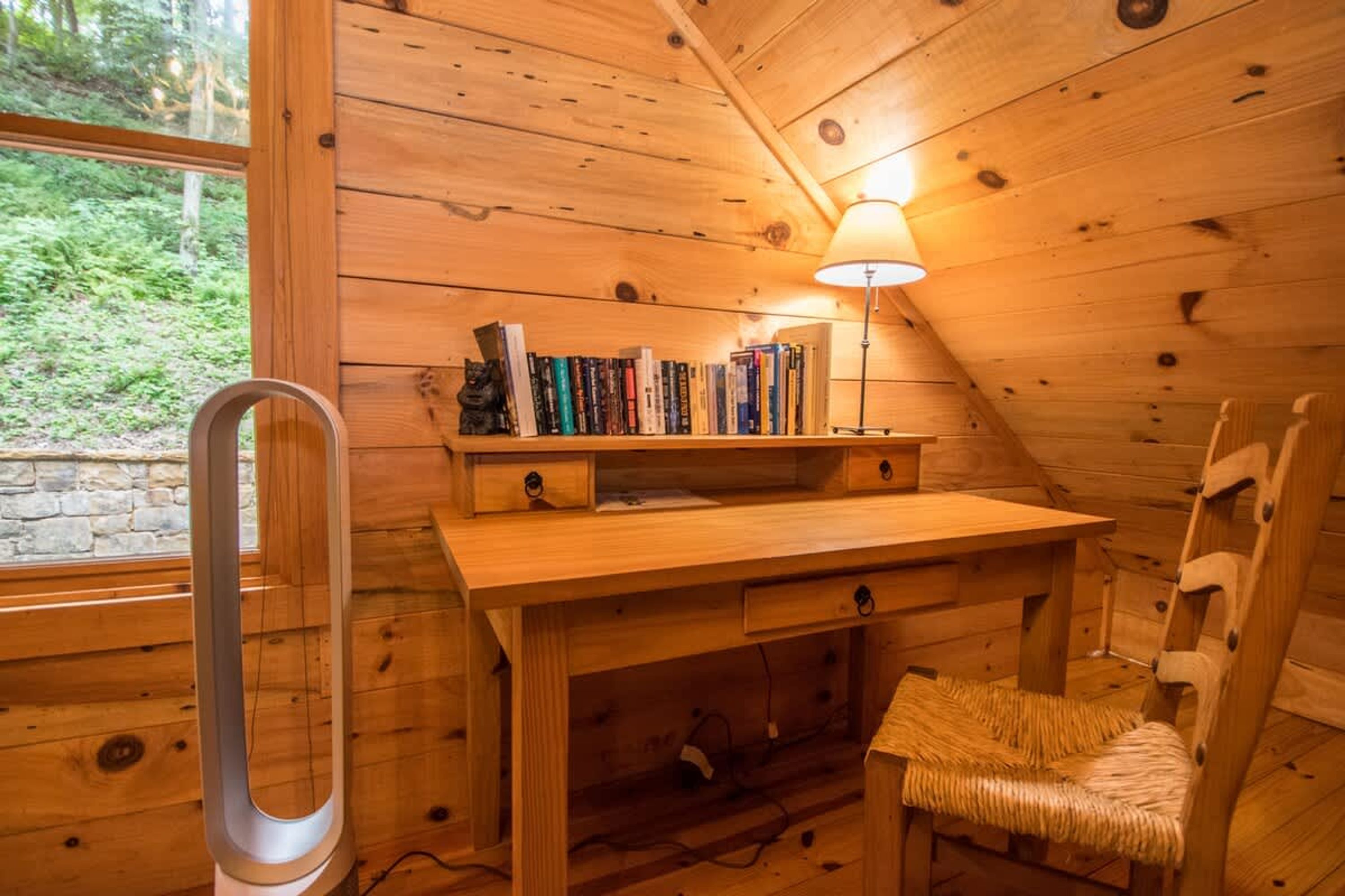 A cozy wooden cabin room with a desk, chair, and bookshelves.