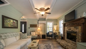 A cozy living room with a fireplace, a ceiling fan, and a large painting on the wall. - Rustic 3BR w Private Pond Firepit Near Trails (Hendersonville)