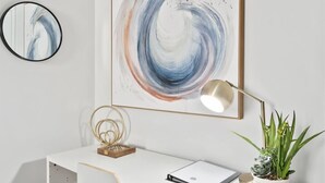 A white desk with a modern lamp, a framed abstract painting, and a potted plant. - Modern 1BR w Workspace Walk to Shops Parks (Asheville)