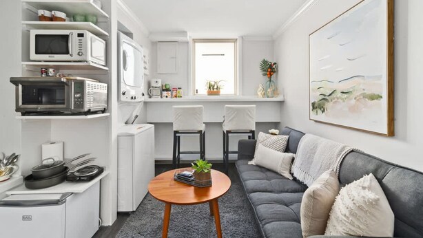 A modern kitchen with built-in appliances, a dining area with two chairs, a gray sofa with cushions, and a large abstract painting on the wall. - Modern 1BR w Workspace Walk to Shops Parks (Asheville)