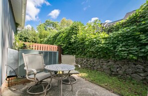 An outdoor patio with a round table and two chairs, a stone wall, and a wooden fence. - Charming 2BR Townhouse w Patio Walk to Main St (Hendersonville)