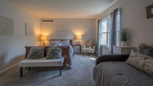 A bedroom with a bed, a bench, a chair, and a bedside table with lamps. - Charming 2BR Townhouse w Patio Walk to Main St (Hendersonville)