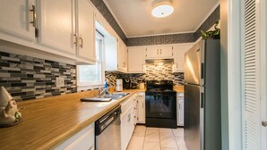 A modern kitchen with white cabinets, a wooden countertop, a black stove, and a stainless steel refrigerator. - Charming 2BR Townhouse w Patio Walk to Main St (Hendersonville)