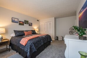 A bedroom with a bed, bedside tables, a dresser, a fan, and a wall with framed pictures. - Charming 2BR Townhouse w Patio Walk to Main St (Hendersonville)