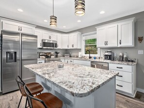 A modern kitchen with white cabinets, stainless steel appliances, a granite island, and pendant lighting. - Spacious 3BR Retreat w Game Room Near Pisgah (Candler)