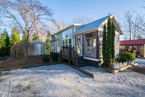 Une maison à deux étages avec un porche couvert, un petit abri de jardin et une allée gravillonnée.