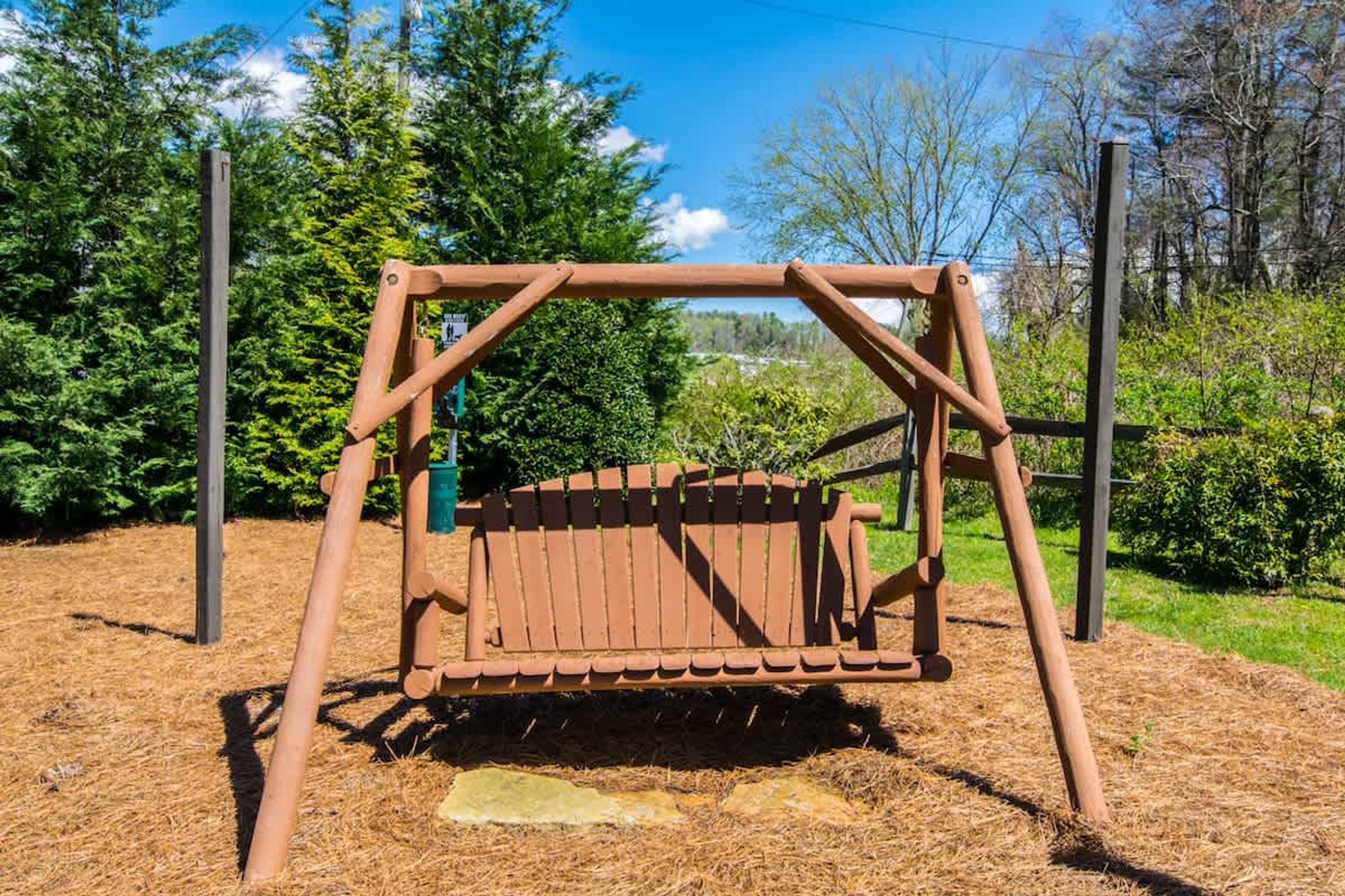 A wooden swing set in a park with a grassy area and trees in the background.