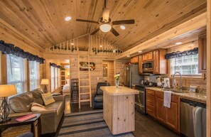A cozy cabin interior with a wooden ceiling, a central island, a kitchenette, and a seating area with a couch and a coffee table. - Lakeview 2BR Tiny Home Near Trails Pool Bocce (Flat Rock)