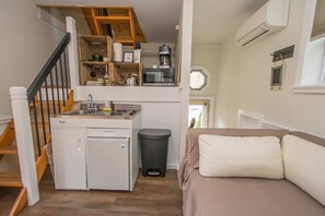 A compact kitchen with a stove, sink, and coffee maker, a small trash bin, and a staircase leading to a loft area. - Dog Friendly Tiny House On Lake Lure Private Dock (Lake Lure)