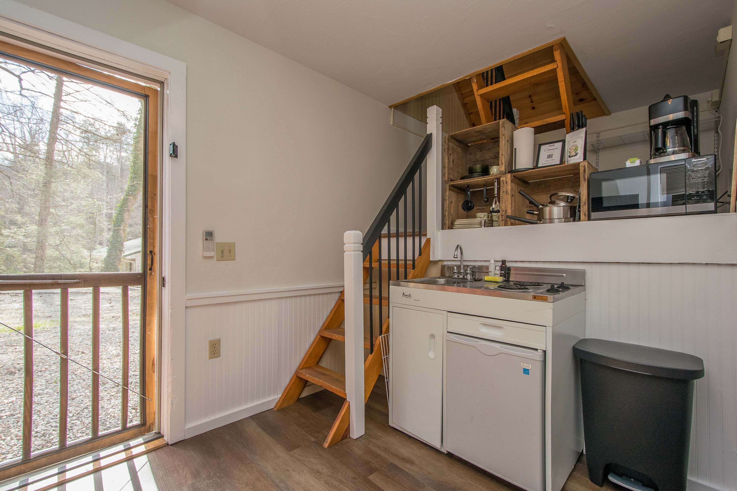 A kitchen with wooden cabinets, a microwave, a coffee maker, and a trash can.