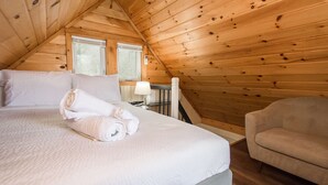 A cozy room with a wooden ceiling, a bed with white linens, a small table with a lamp, and a chair. - Dog Friendly Tiny House On Lake Lure Private Dock (Lake Lure)
