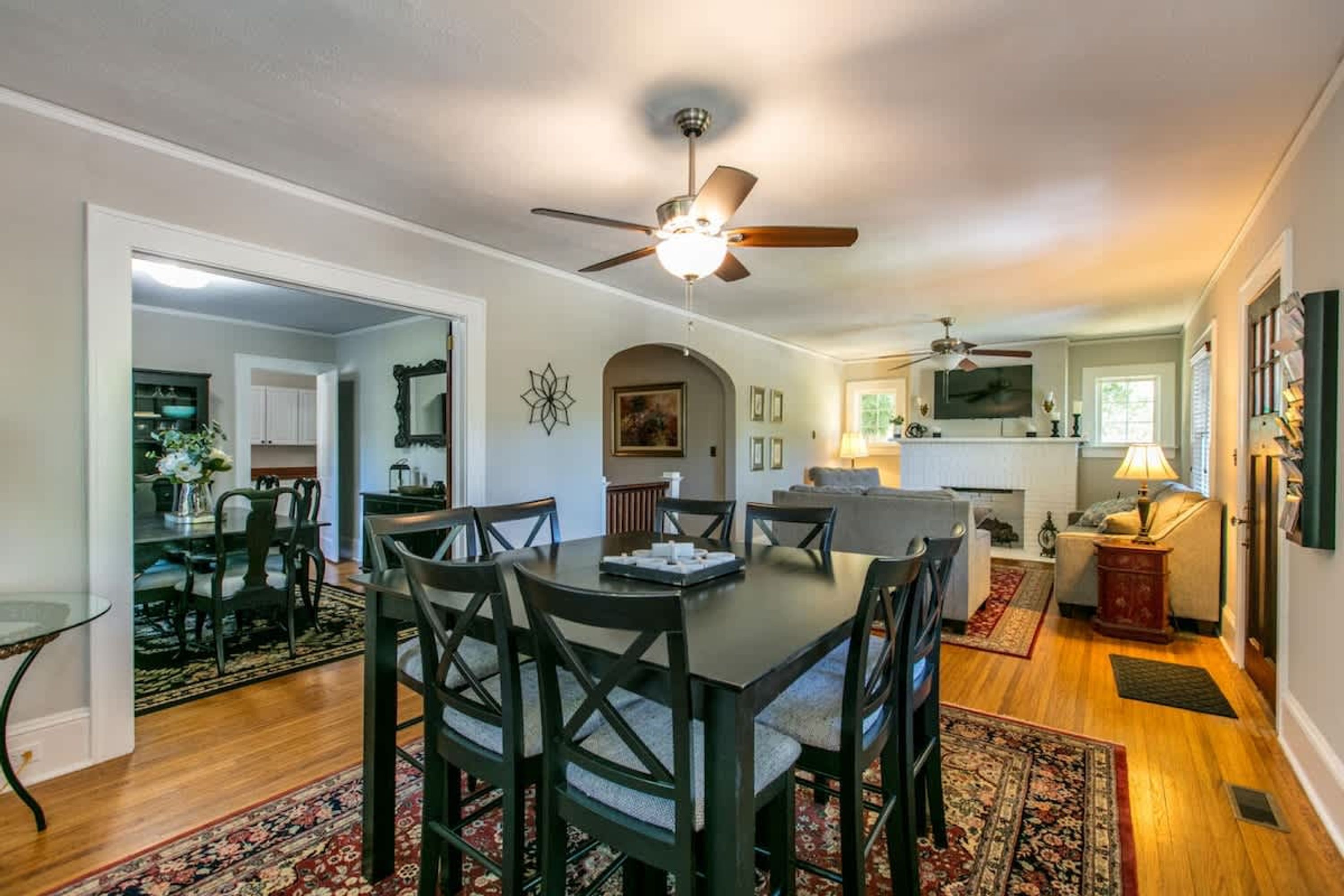 A spacious dining area with a dark wooden table and chairs, a ceiling fan, and a view into the kitchen.