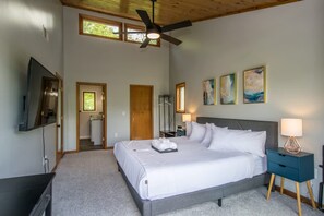 A bedroom with a large bed, a ceiling fan, a TV, and artwork on the wall. - Mountain View 3BR w Sunroom Close to Ski Trails (Maggie Valley)