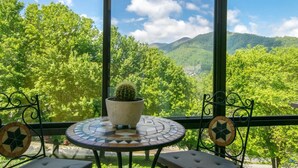 Een balkon met een ronde tafel, een cactus in pot en uitzicht op een groen landschap met bomen en bergen.