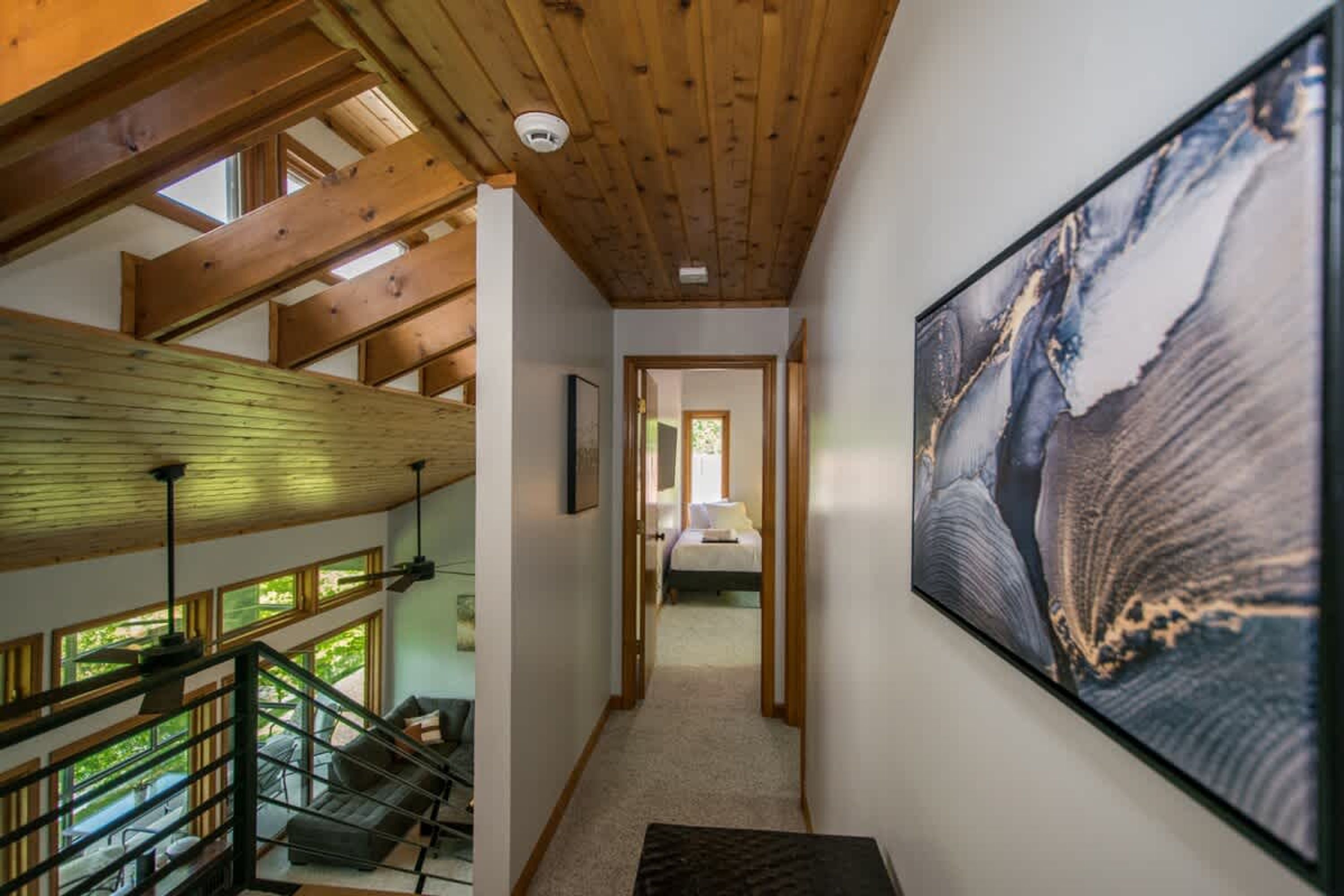 A spacious interior with a high ceiling, wooden beams, a staircase, and a large framed artwork on the wall.